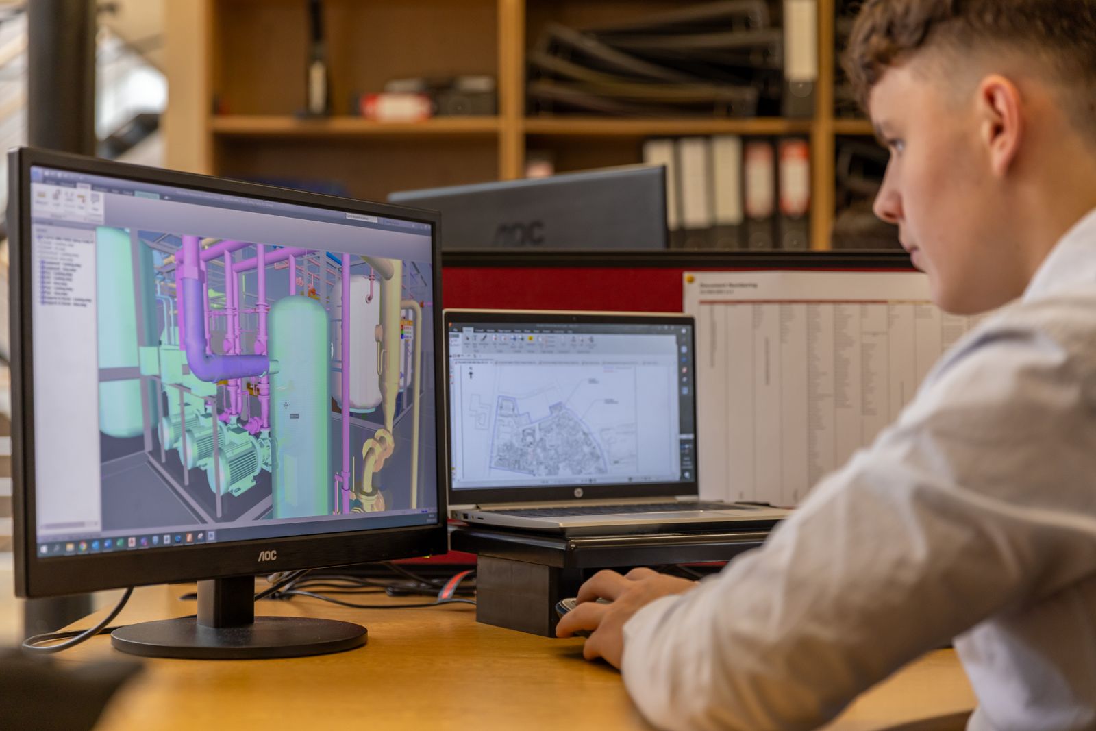 Engineer working on a 3D plant model in CAD software at a dual-monitor workstation