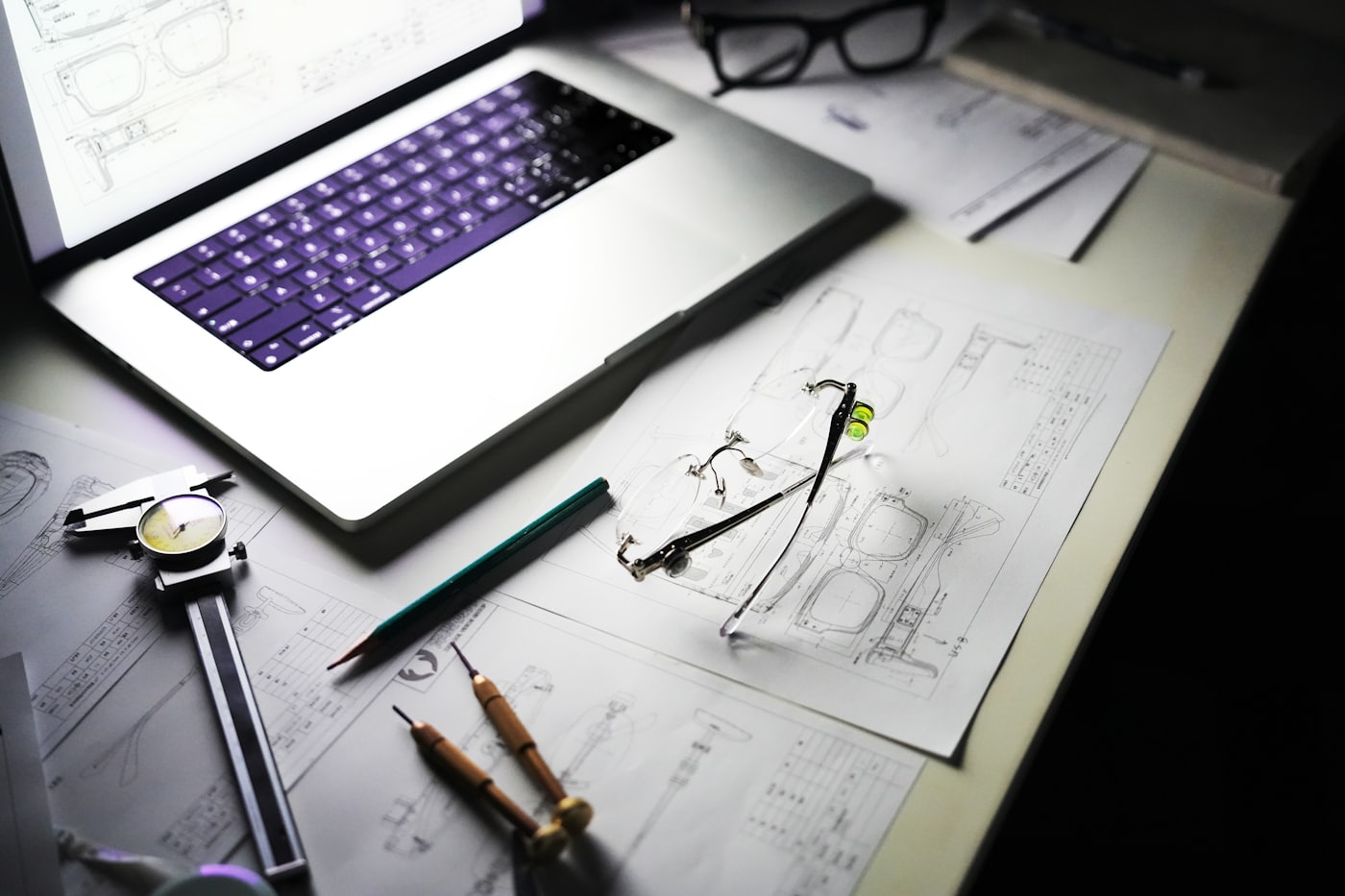 Technical drawings of a product with drafting instruments and a metal prototype on a desk