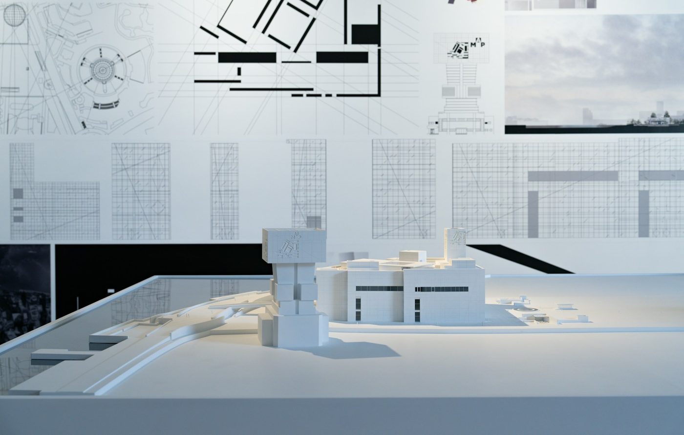 A scale architectural model displayed in front of mounted building drawings